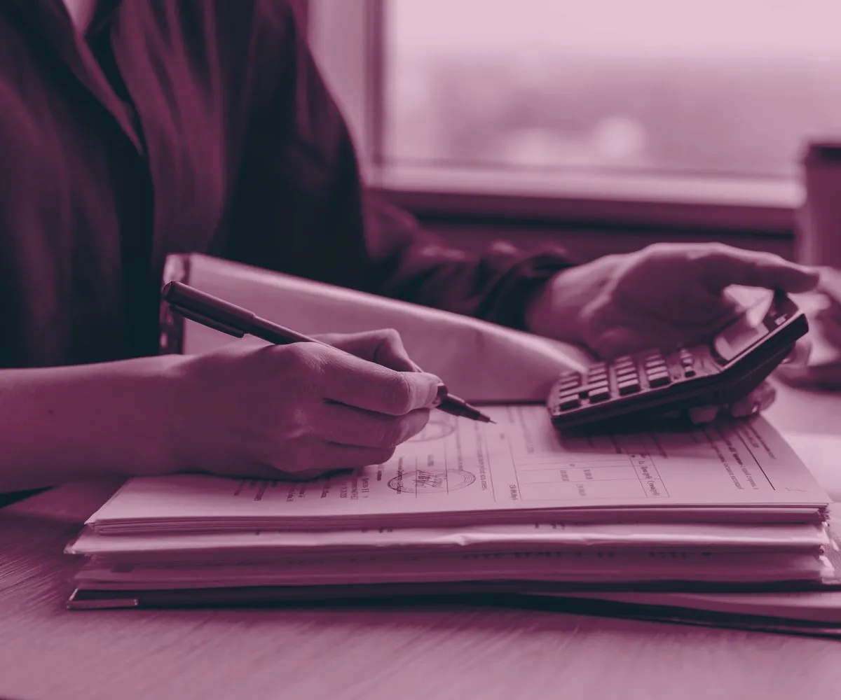 Mãos conferindo uma pilha de documentos de crédito, com caneta e calculadora sobre a mesa